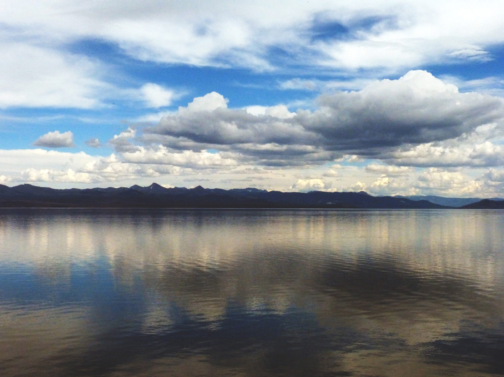 A massive sky few of clouds reflects onto an equally massive lake.