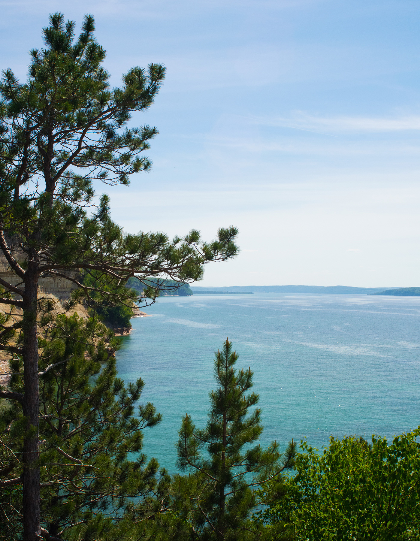 The turquoise coastline of Pictured Rocks, MI is framed by trees.
