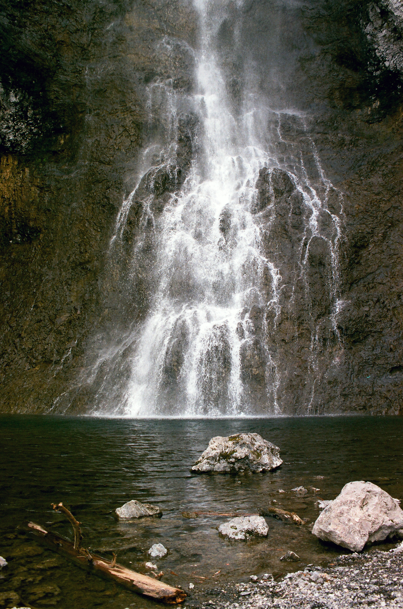 A shower of water gracefully drifts down a rock face to meet a small reservoir.