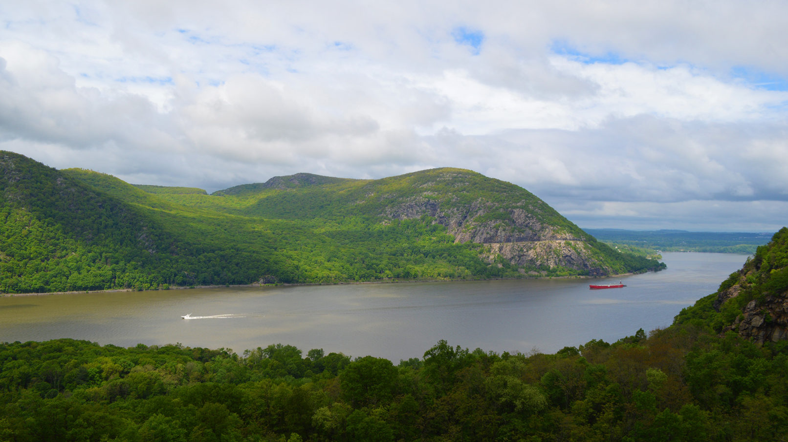 Two boats crossing the Hudson River are dwarfed by foothills.